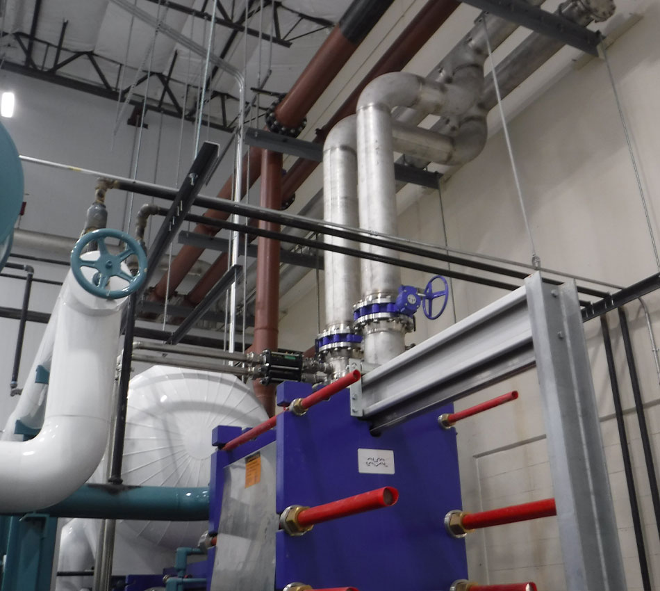 Pipes and valves connect to blue heat exchanger in mechanical room.