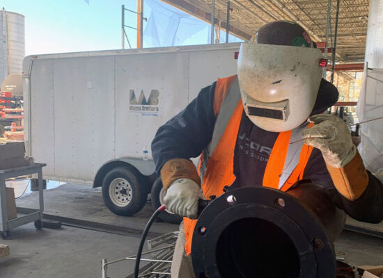 Worker in helmet welds large pipe at construction site.