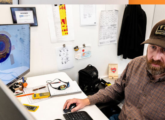 Man in brown cap works at desk with 3D model.