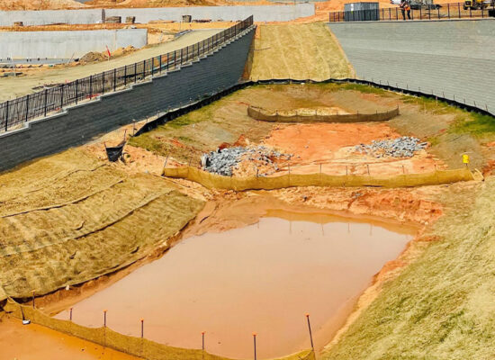Muddy pond, sloped banks, retaining walls, fences, vehicles, materials.