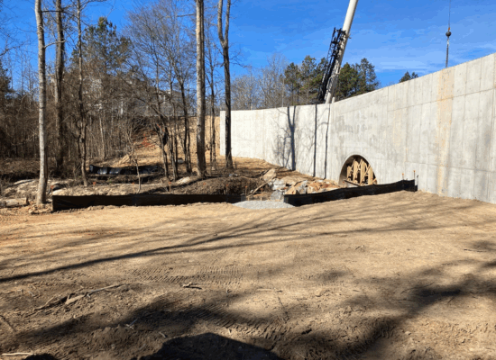 Construction site with crane, concrete wall, silt fence, trees.