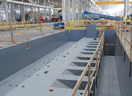 Unfinished rectangular pit with railings, workers and equipment nearby.
