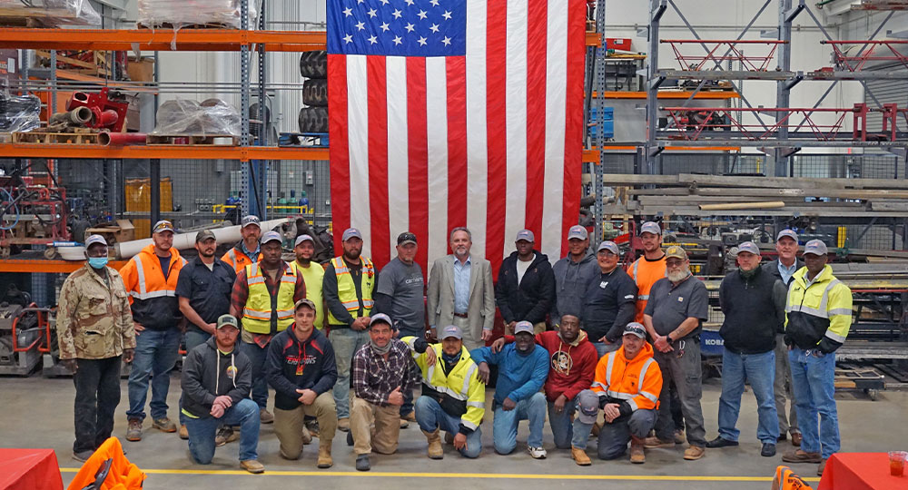 Workers pose by large American flag inside warehouse.