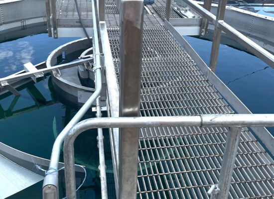 Metal walkway spans circular water tank with blue water.