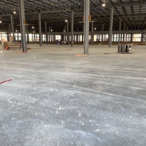 Unfinished industrial interior with concrete floors, steel columns, scattered materials.