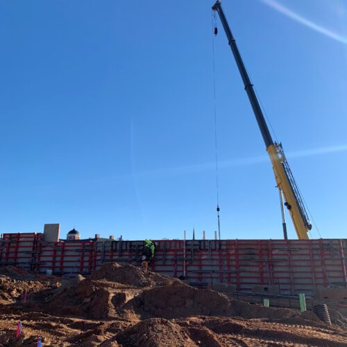 Crane lifting materials at construction site, dirt piles foreground.