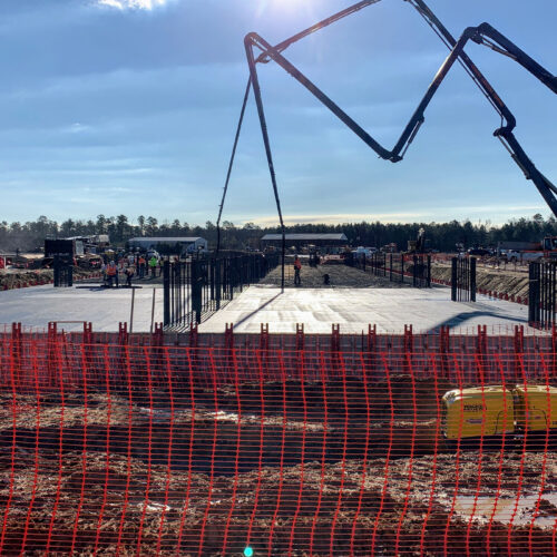 Workers pour concrete slab at construction site with safety fencing.