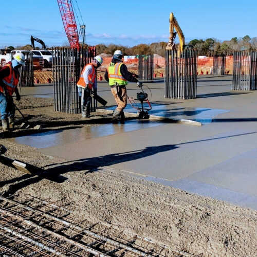 Workers smooth concrete foundation at outdoor construction site.
