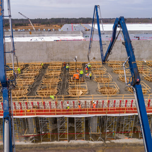 Aerial view: workers pour concrete onto framework under cloudy skies.