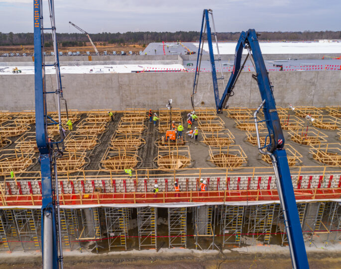 Aerial view: workers pour concrete onto framework under cloudy skies.