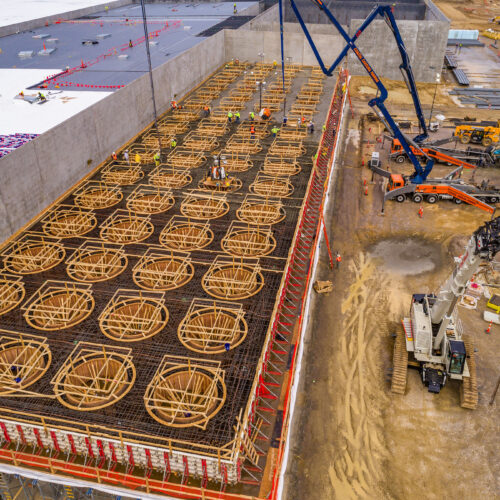 Aerial shot of workers, cranes, and machinery at building site.