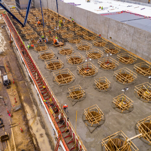 Aerial view of workers building circular forms beside tall building.