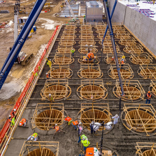 Workers pour concrete into circular forms at a site.