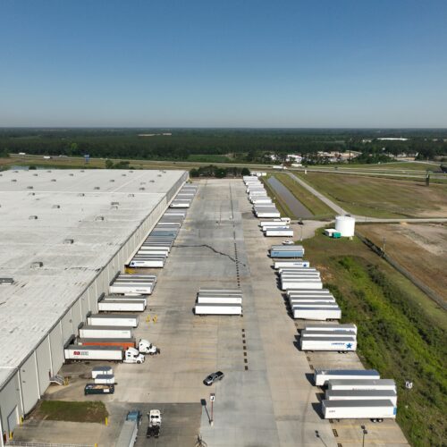 Warehouse with many semi-trailers at docks, fields and factories nearby.