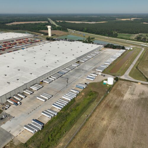 Aerial view of warehouse, loading docks, trucks, fields, highway.