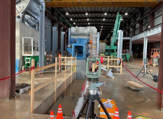 Indoor construction site with surveying gear, cones, railings, machinery.