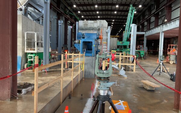 Indoor construction site with surveying gear, cones, railings, machinery.