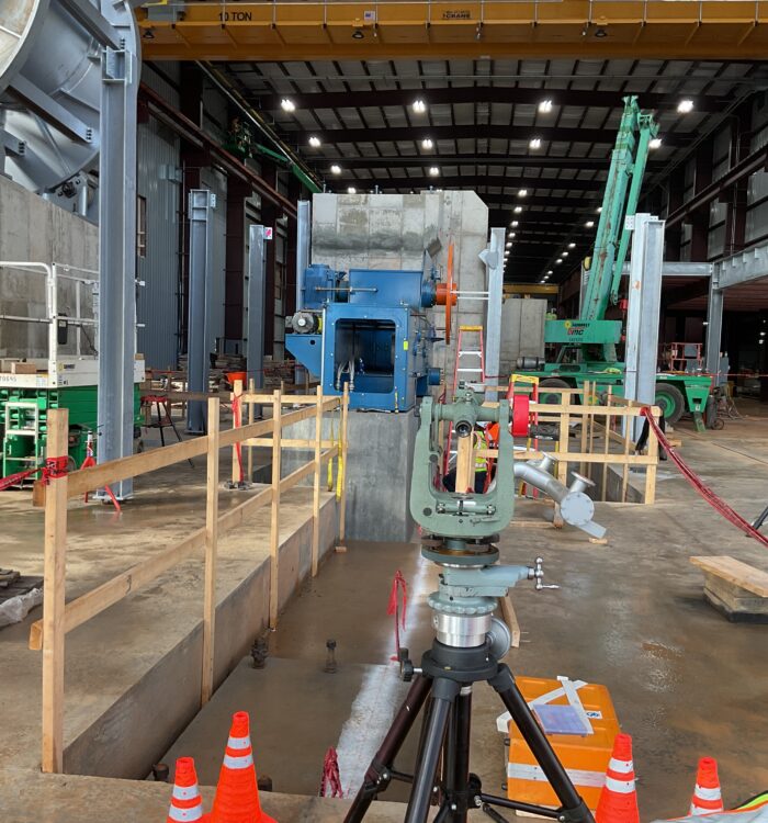 Indoor construction site with surveying gear, cones, railings, machinery.