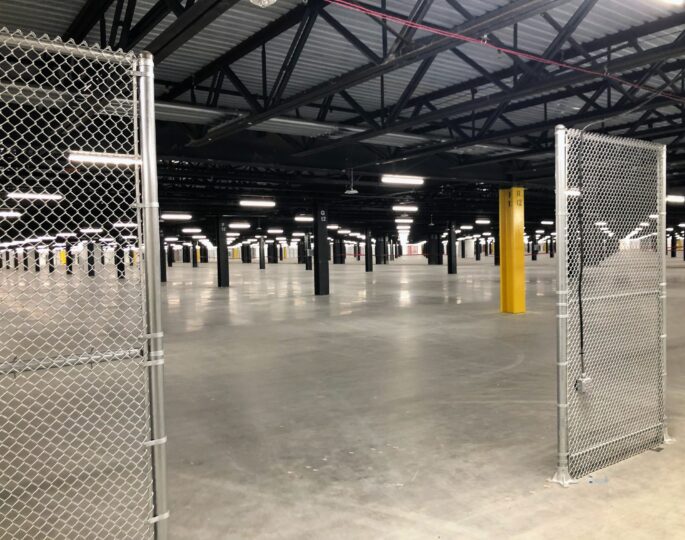 Empty industrial space with concrete floor, beams, chain-link gate.