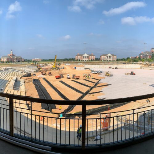 Stadium construction scene with machinery, workers, and unfinished seats.