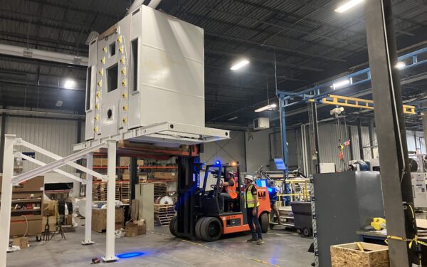 Workers use a forklift to move a large machine in a warehouse.