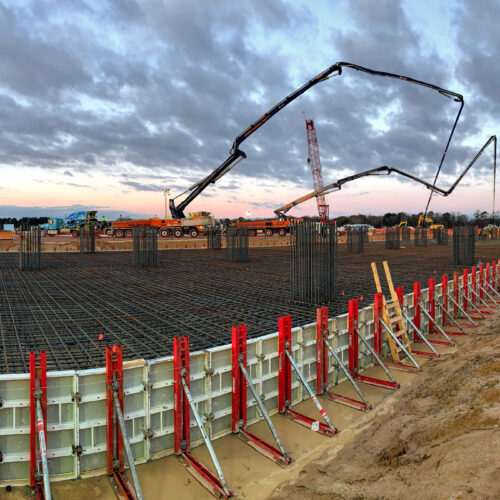 Construction site at sunset with rebar, formwork, and boom pumps.
