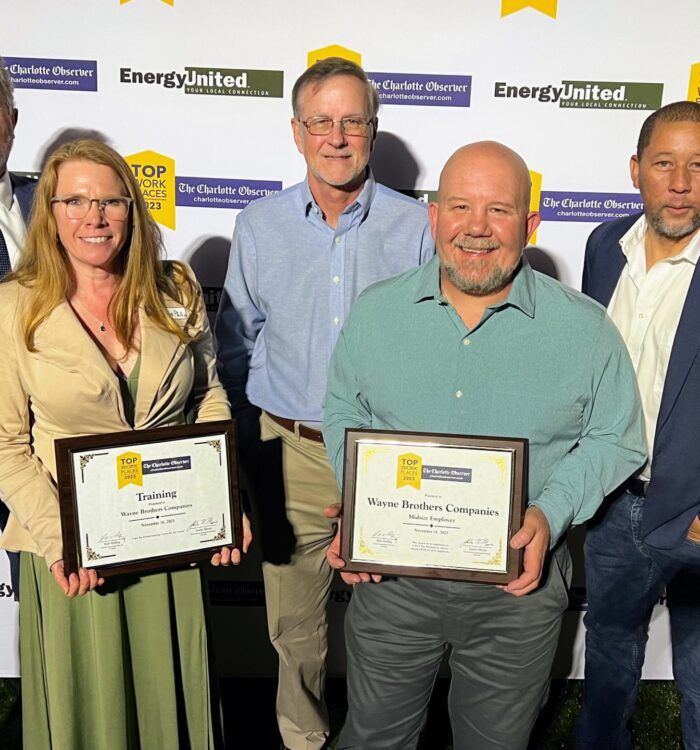 Five people pose at an award event; two hold framed certificates.