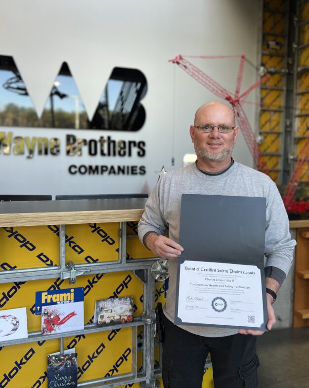 Man holding certificate by Wayne Brothers sign in office.