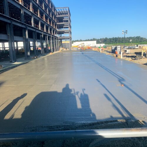 Concrete slab being poured and leveled at construction site.