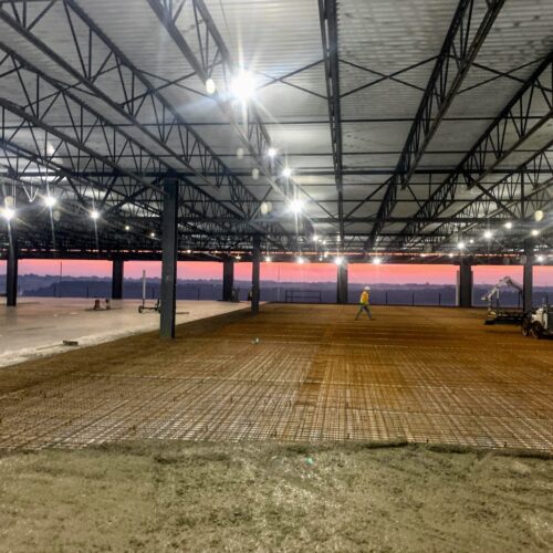 Industrial building under construction, workers present, sunset in background.