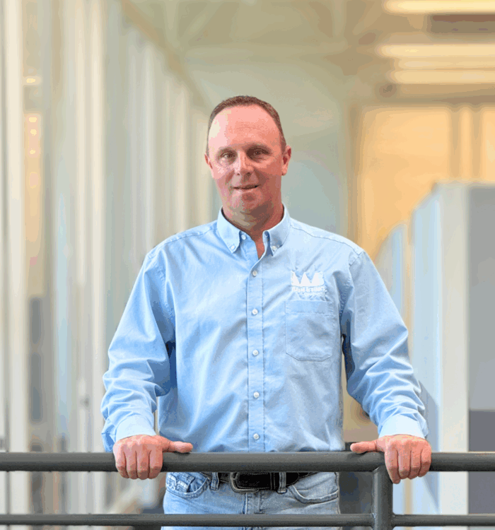 Man in blue shirt holds railing indoors; office background blurred.