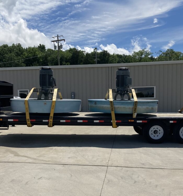 Flatbed trailer with two industrial tanks and pallet, parked outside.
