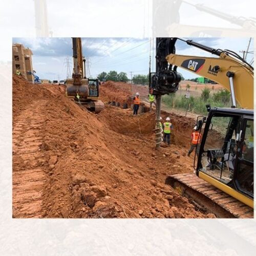 Workers use excavators at a dirt site near utility poles.