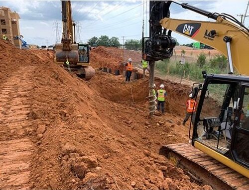 Workers use excavators at a dirt site near utility poles.