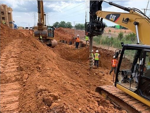 Workers use excavators at a dirt site near utility poles.