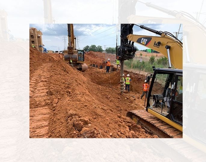 Workers use excavators at a dirt site near utility poles.