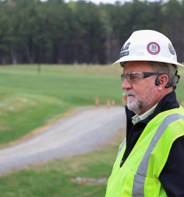 Man in hard hat and safety vest stands by gravel path outdoors.