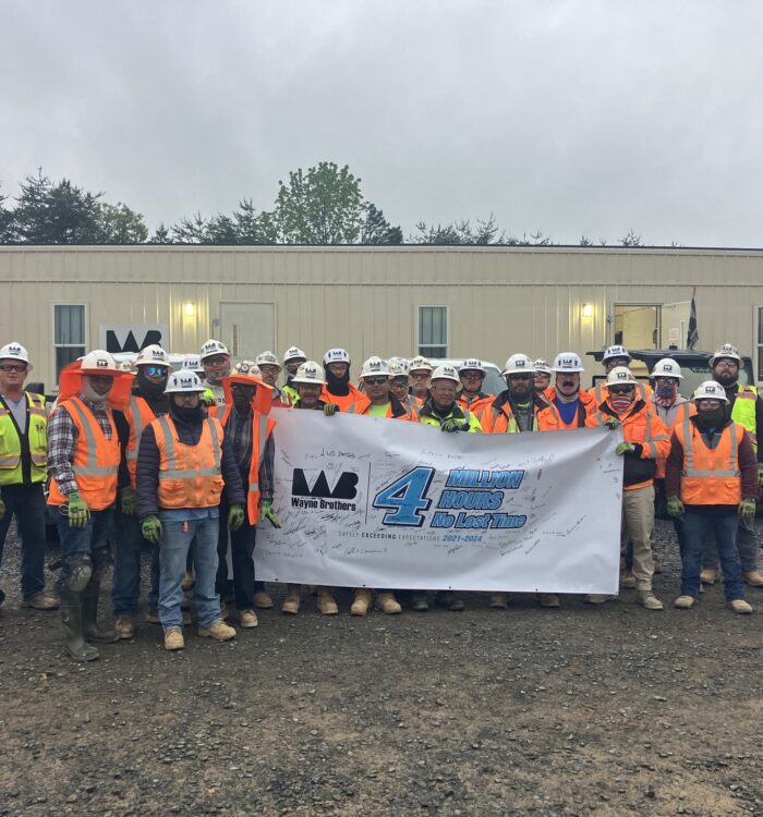 Construction workers hold 4 million hours safety banner by trailer.
