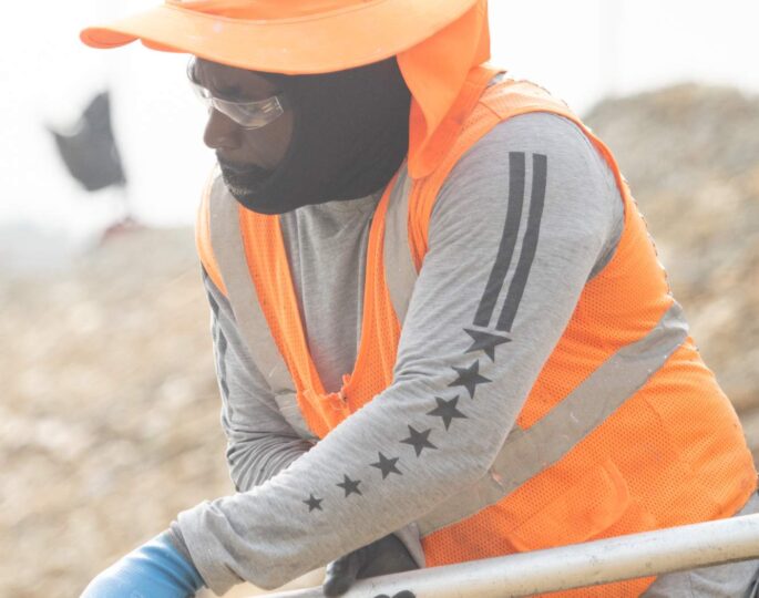 Construction worker in orange vest and helmet uses long tool.