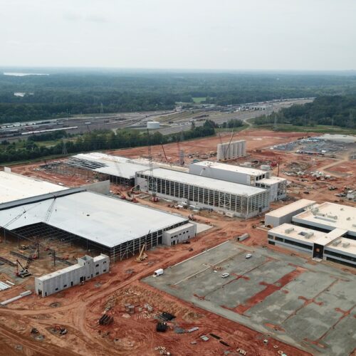 Aerial of industrial site amid red earth, forest, and roads.
