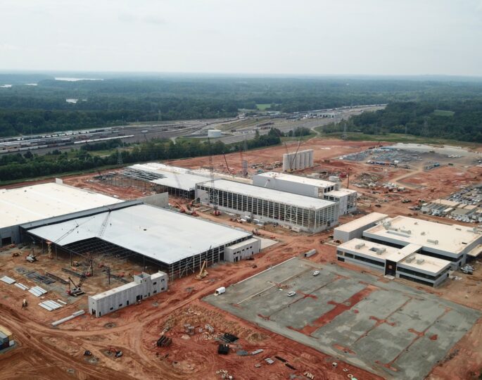 Aerial of industrial site amid red earth, forest, and roads.