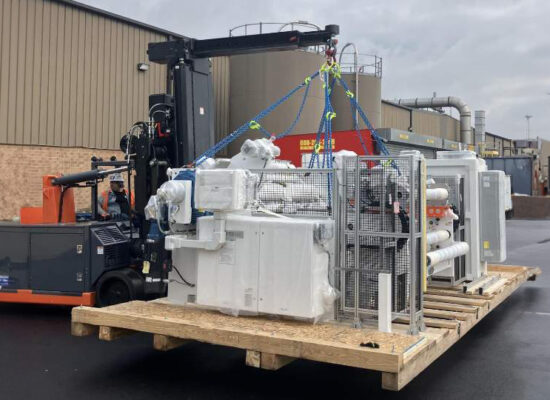 Forklift moves industrial equipment on pallet outside warehouse.