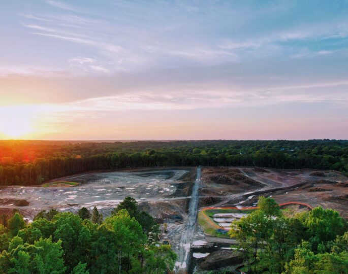 Aerial view of sunset construction site with dirt and trees.