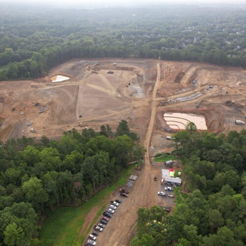 Aerial view: cleared construction site, dirt paths, ponds, forest.