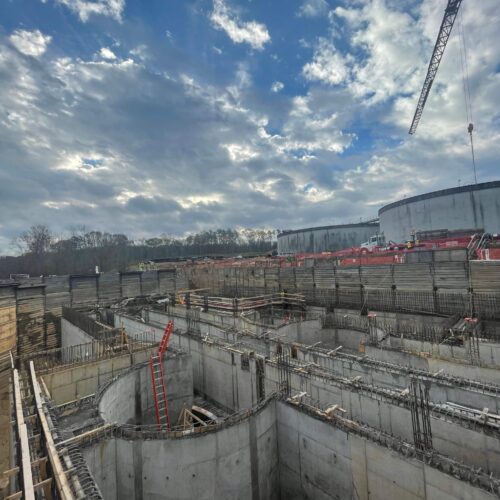 Construction site with concrete bases, steel bars, red ladder, crane.